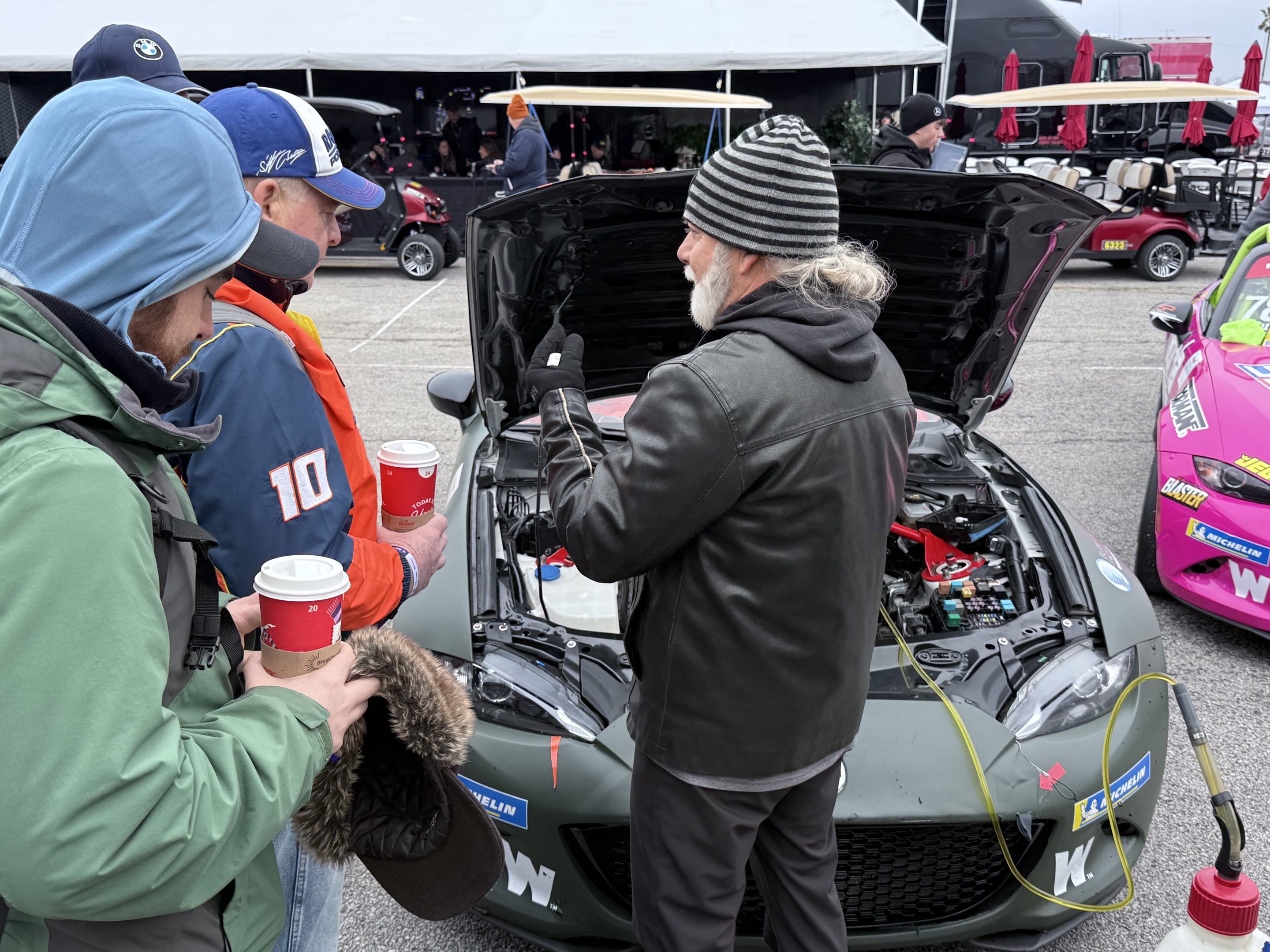 Men standing coldly around a small race car><img src=